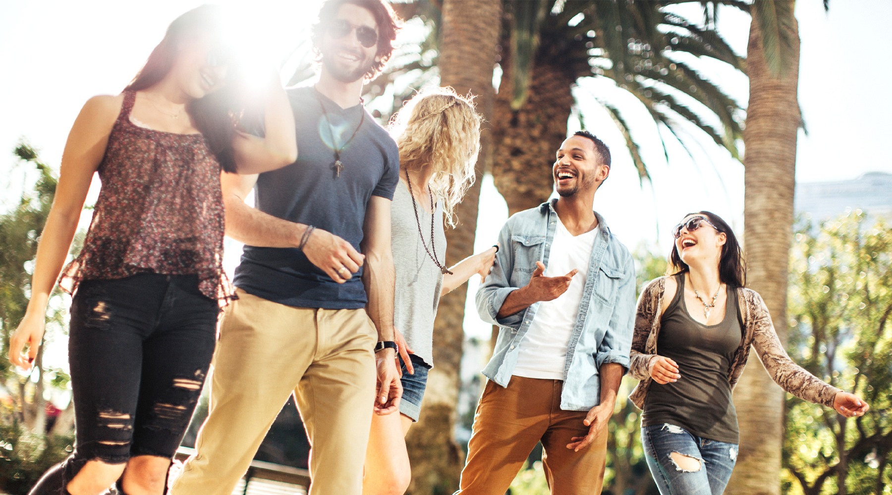 A group of friends hanging out and laughing surrounded by palm trees.